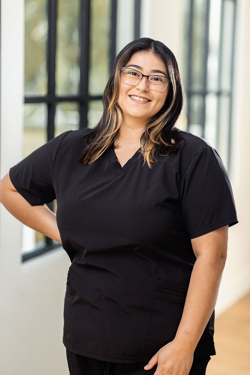 Smiling woman in black scrubs, standing indoors.