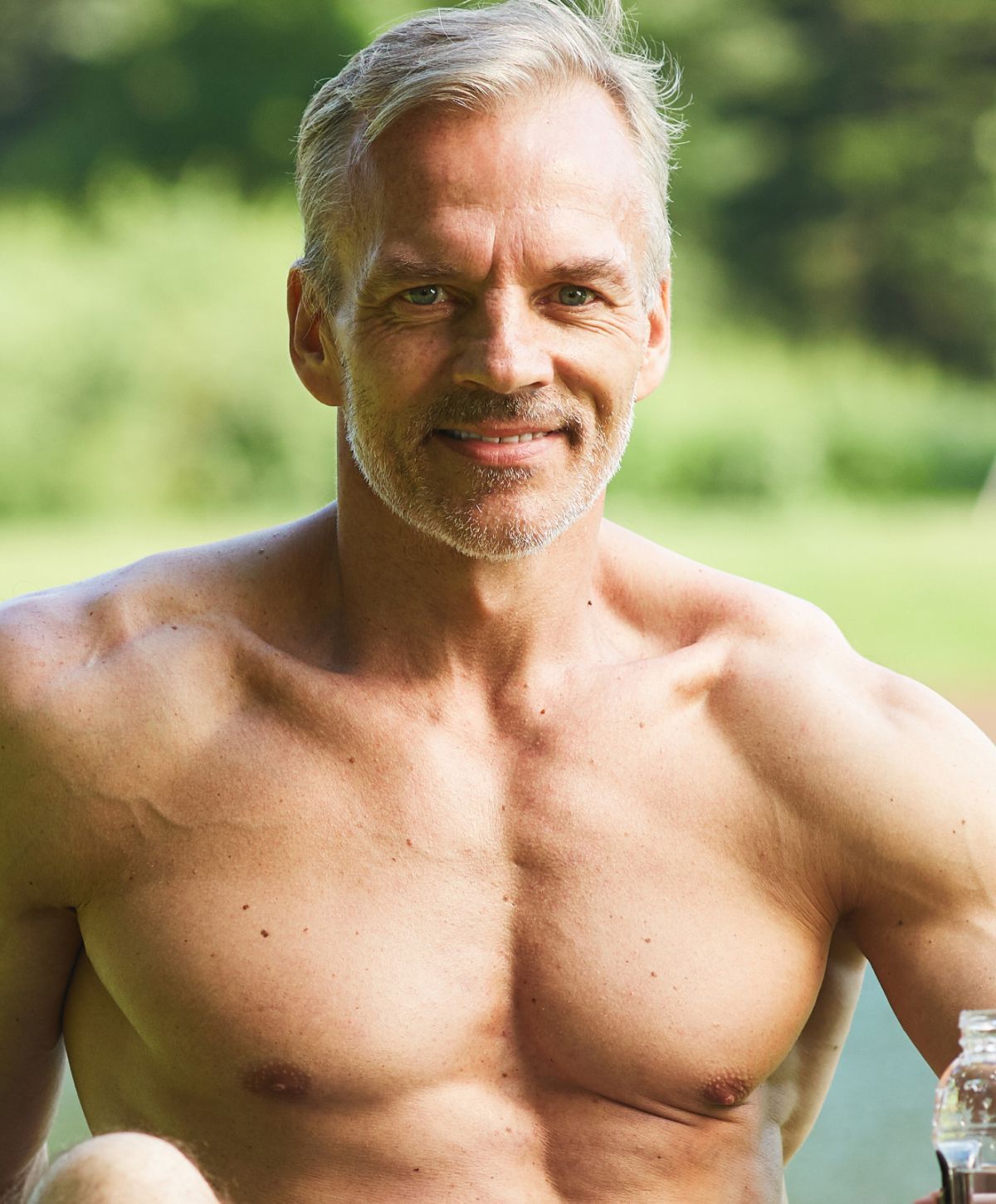 Fit older man smiling outdoors by water.